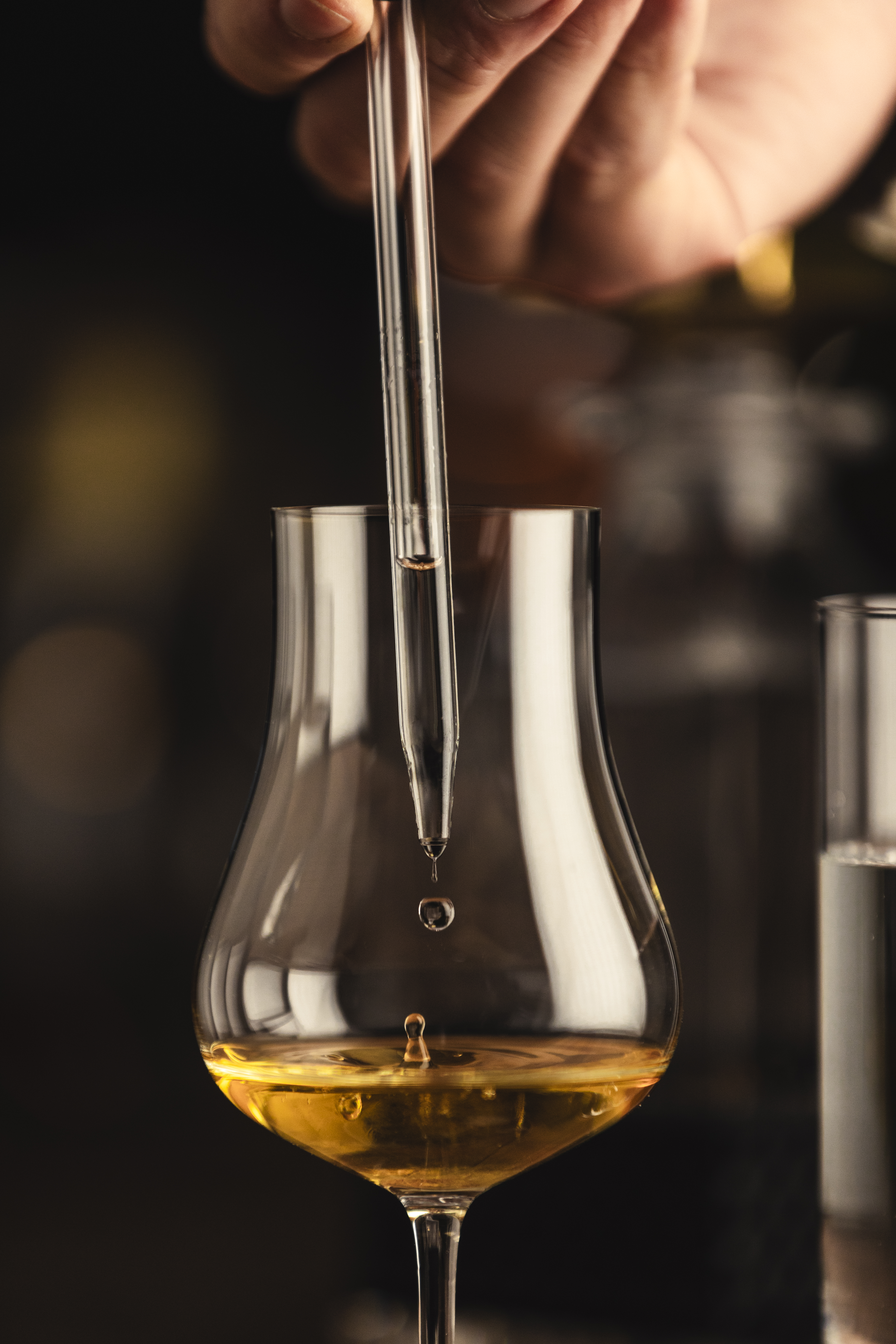 Zufügen von Wasser in ein Spirituosenglas durch eine Whiskypipette