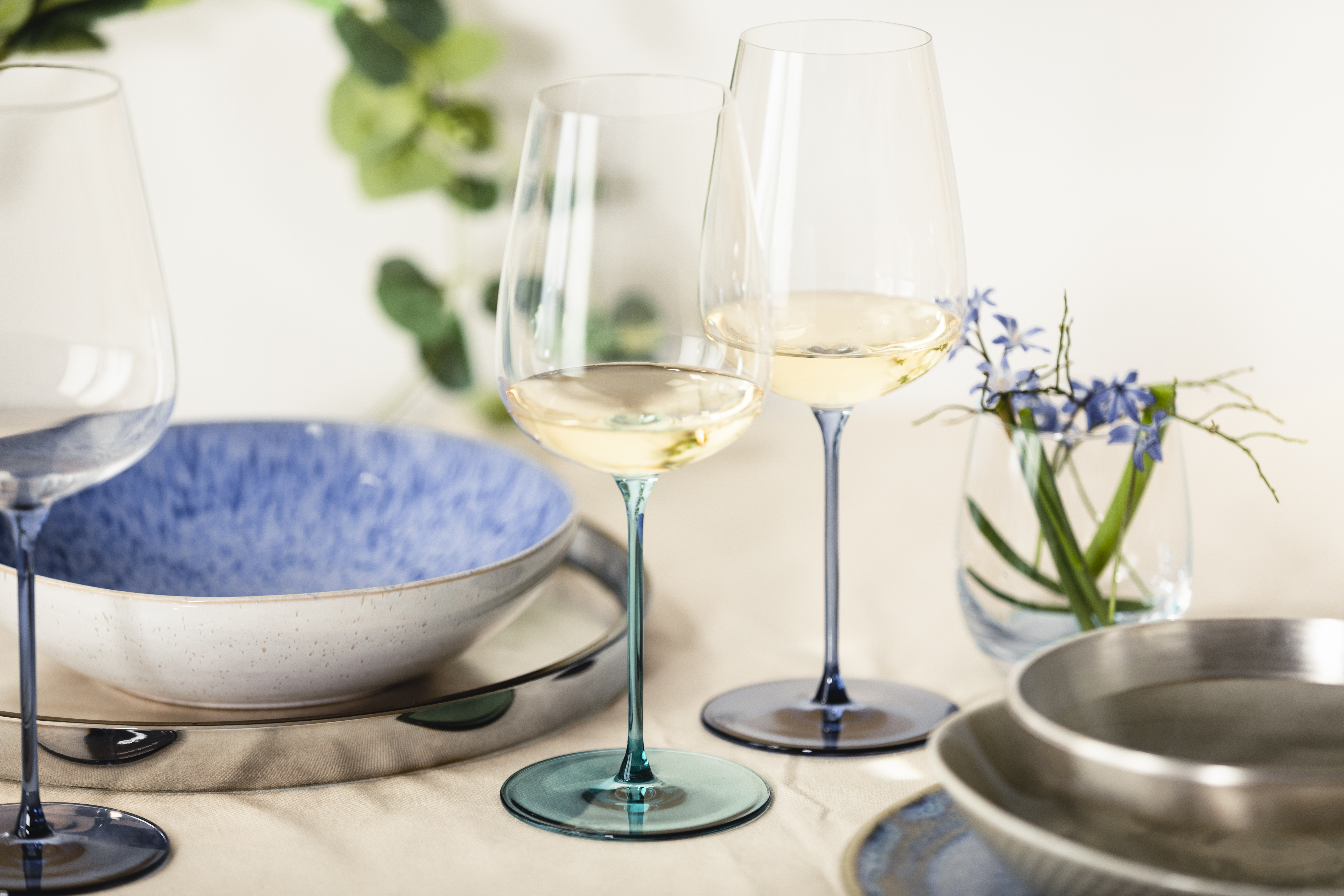 Three wine glasses in shades of blue filled with white wine