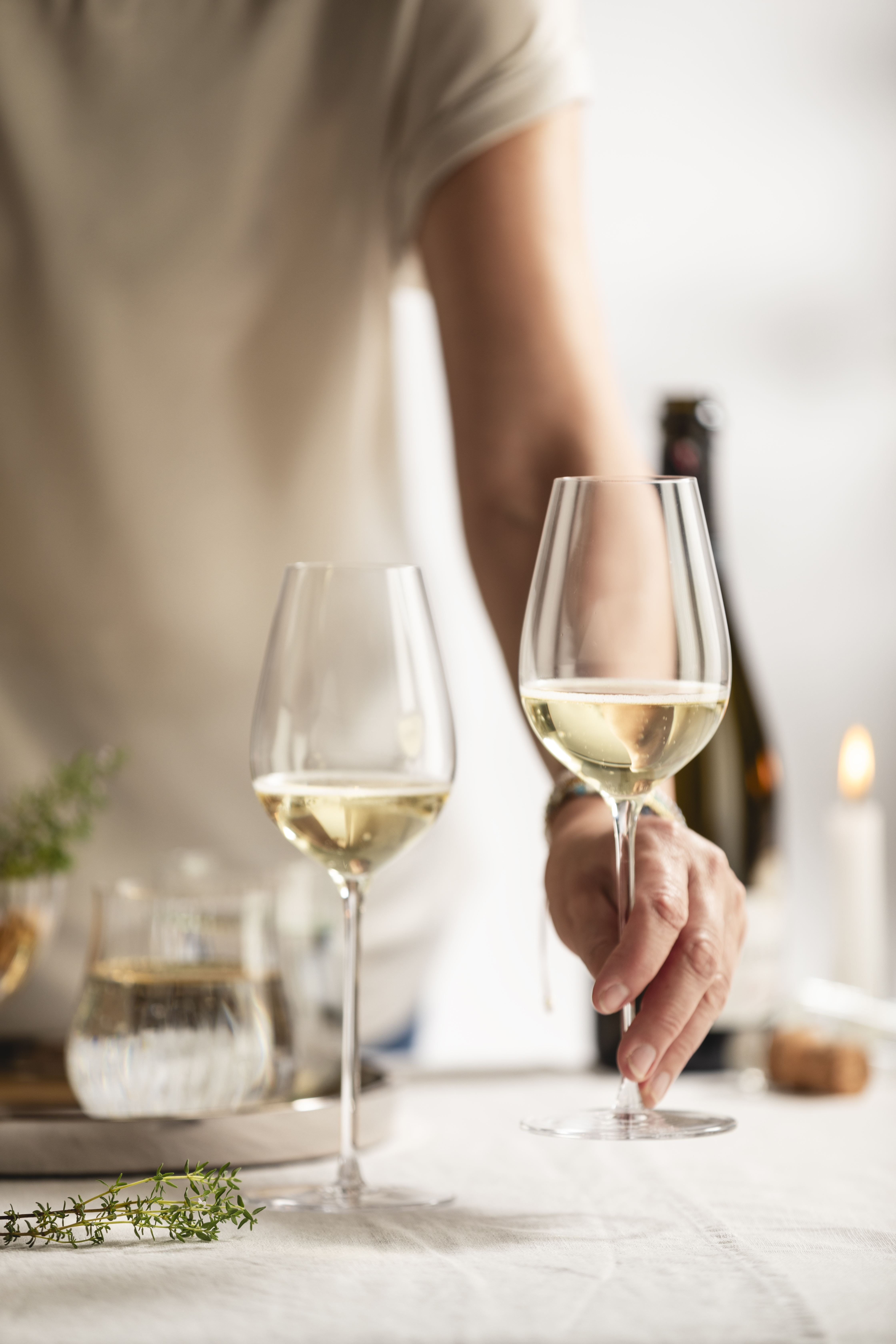 A hand places a second white wine glass on a table