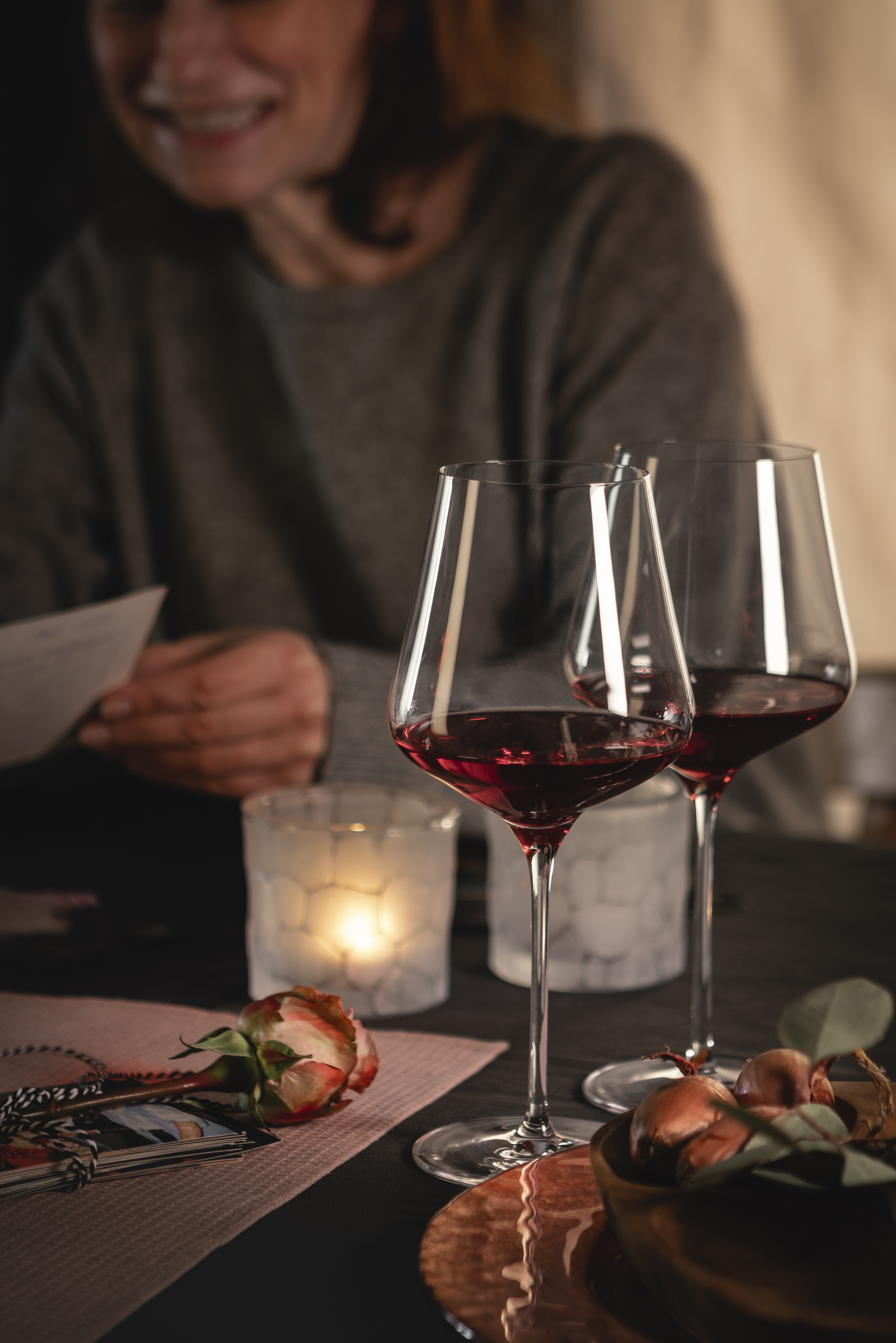 A smiling person sits at a table with two wine glasses and candlelight