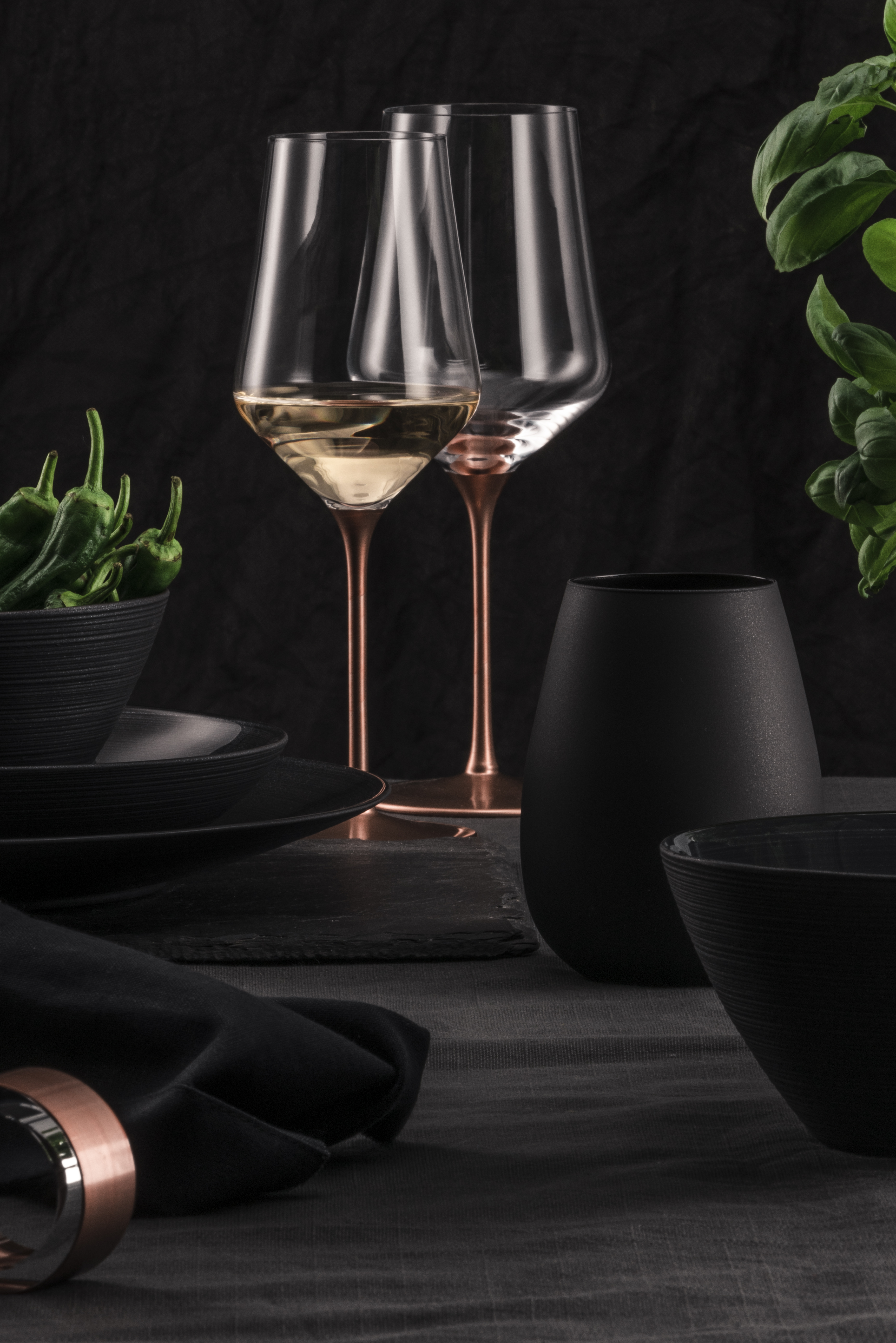 Two white wine glasses with copper stems in a black/green setting