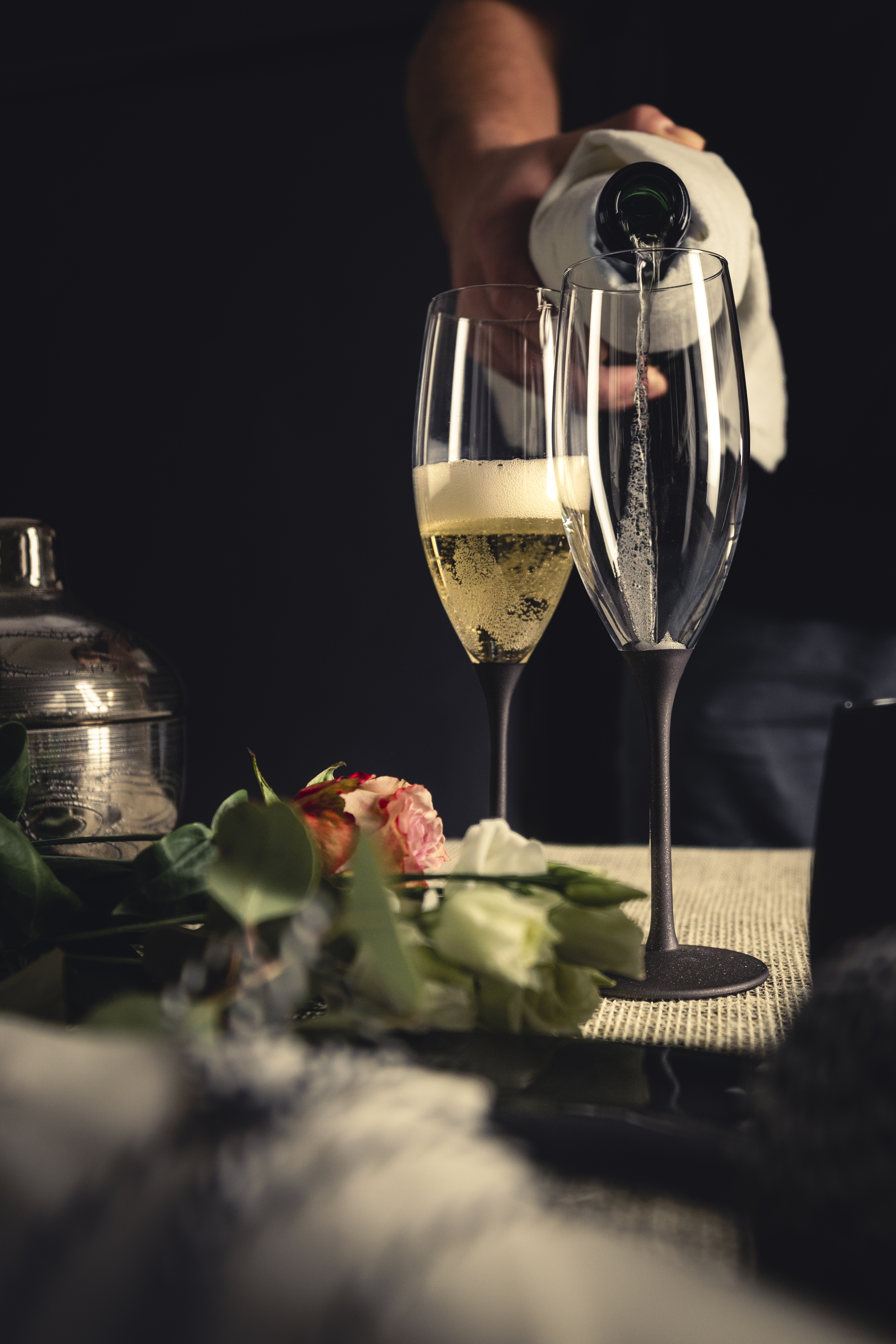Two champagne glasses with black bases and platinum tin in the background