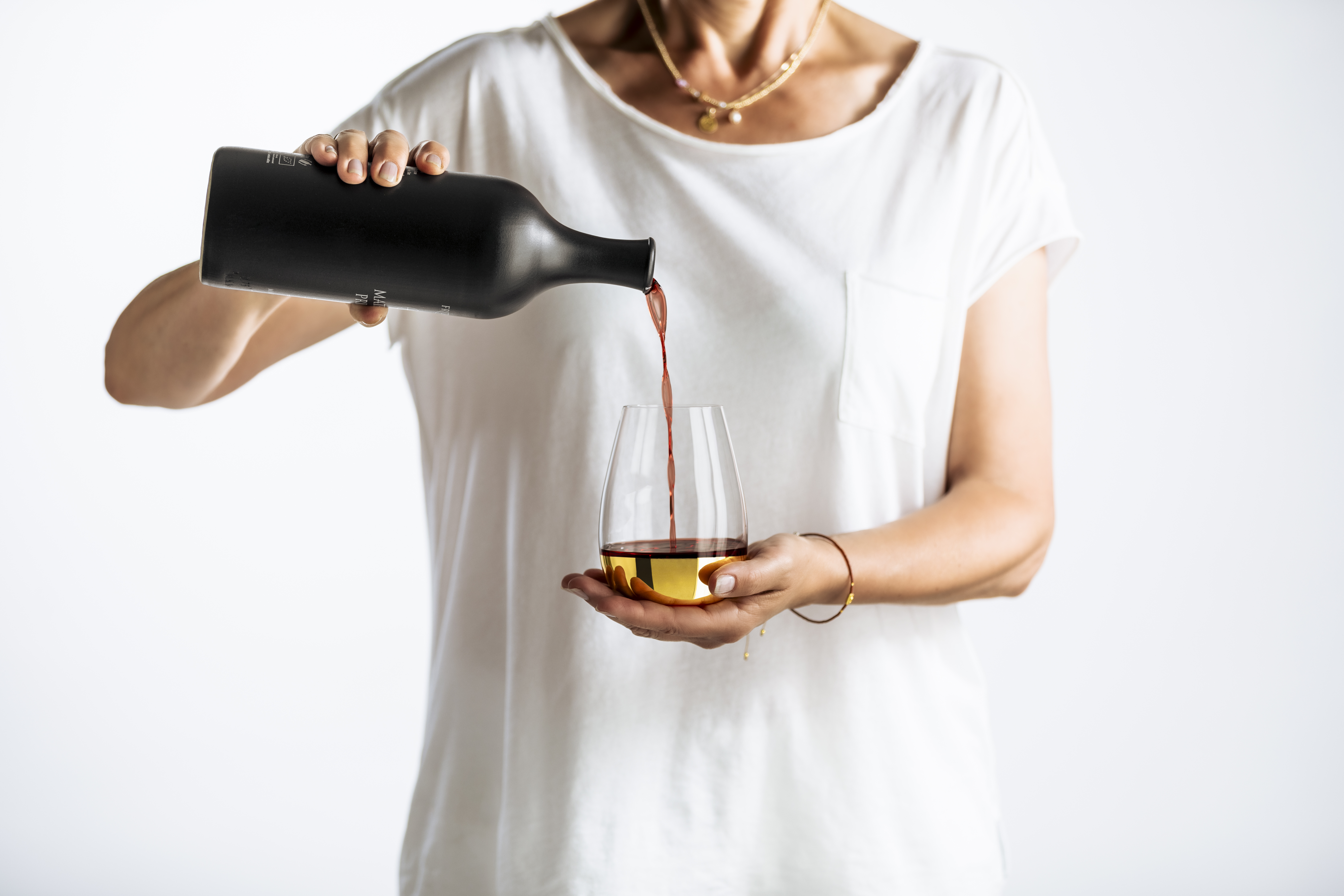A person pours wine into a gold glass from the Elevate series.