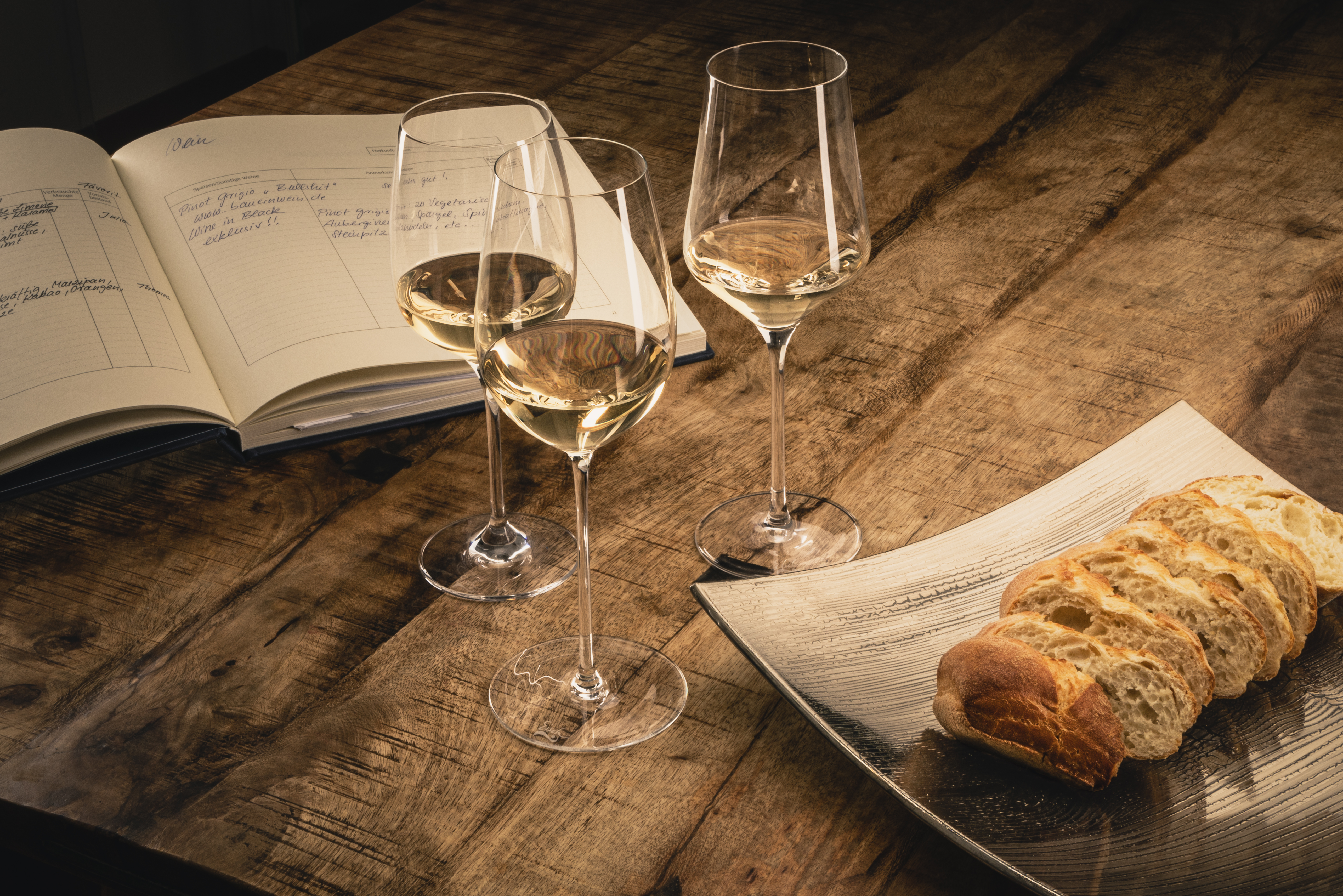 Three white wine glasses with baguette on a table