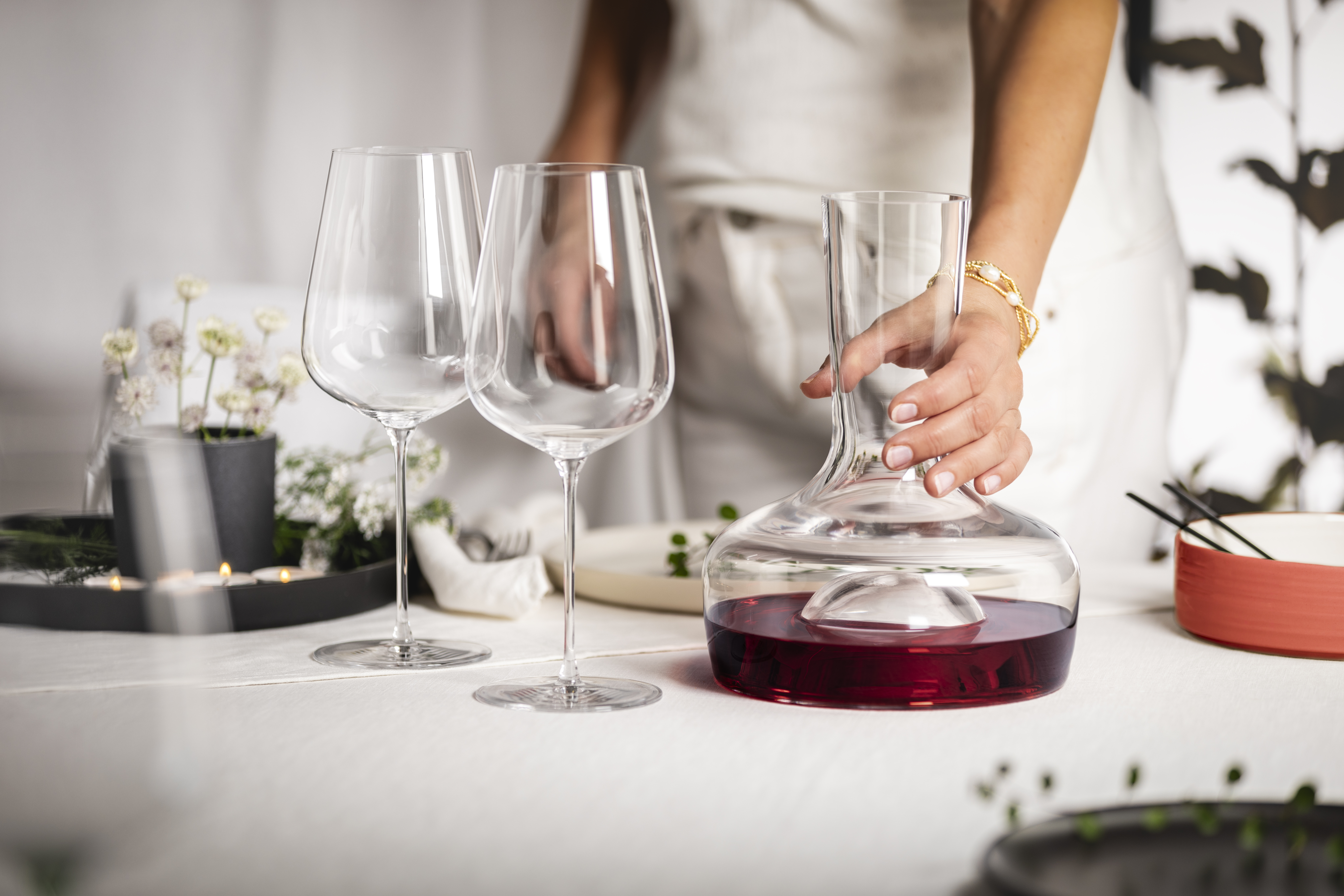 Hand holding a decanter on a table next to two wine glasses