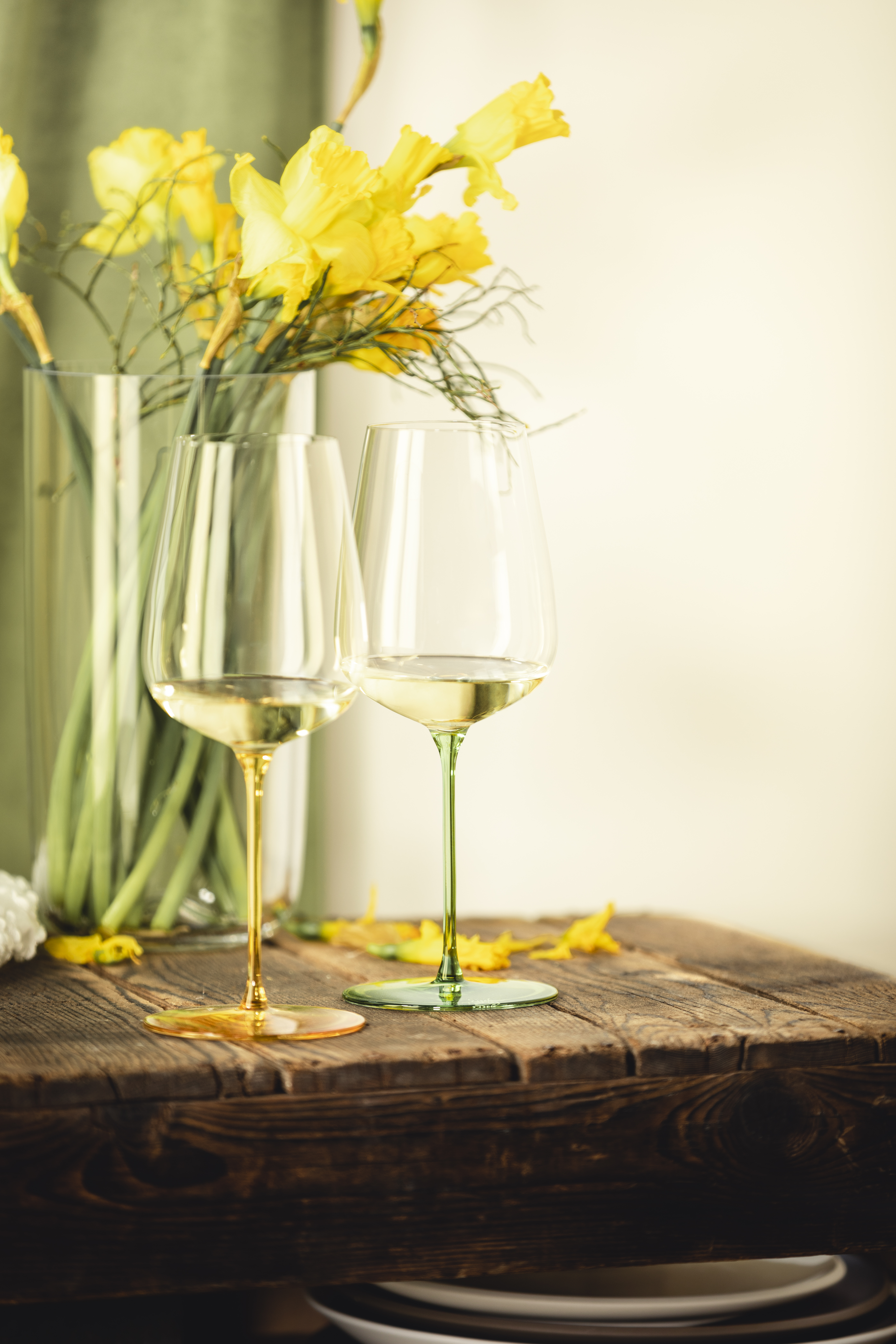 Two wine glasses in yellow and green in front of a yellow bouquet of flowers