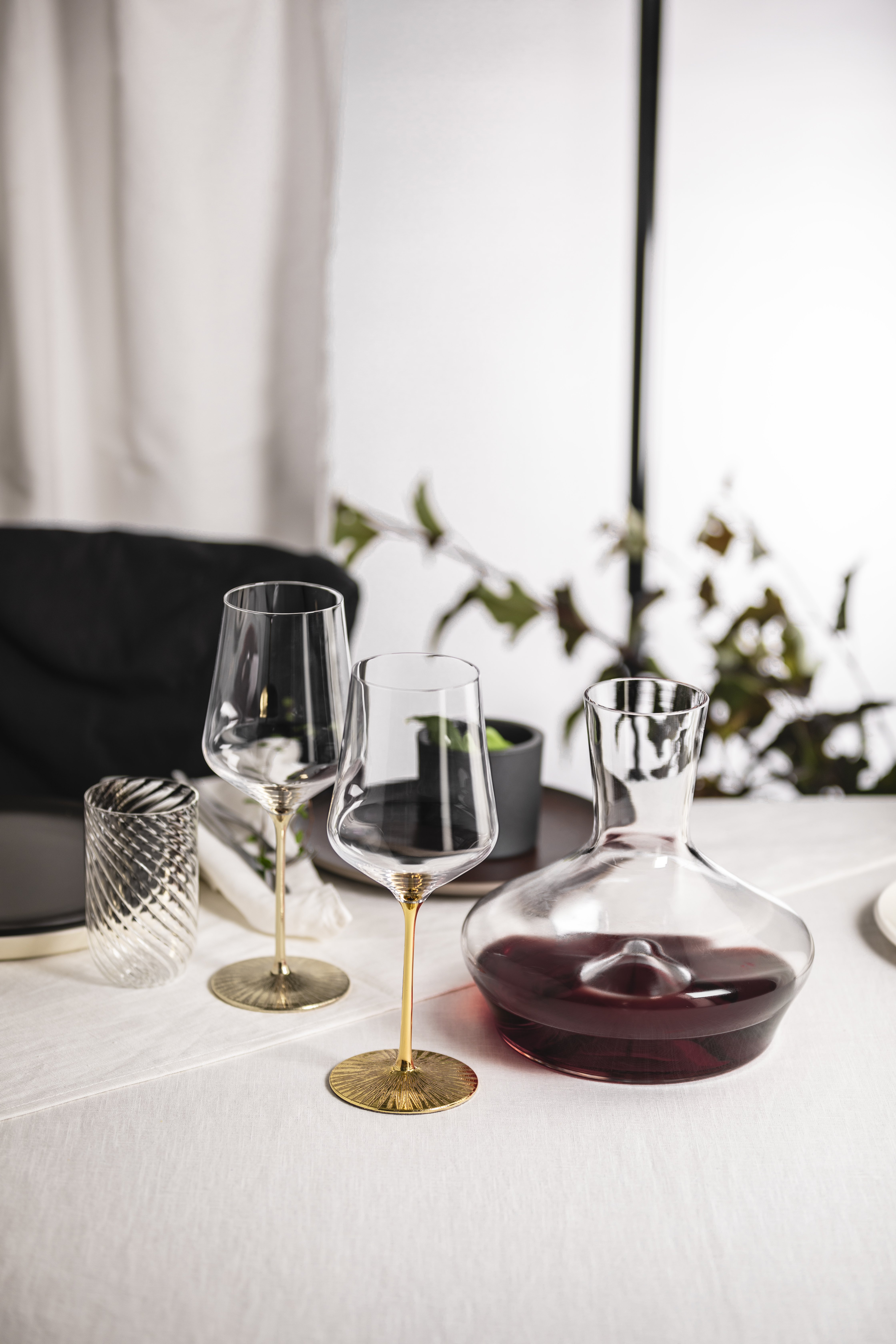 Two Bordeaux glasses in gold and silver with a decanter on a table