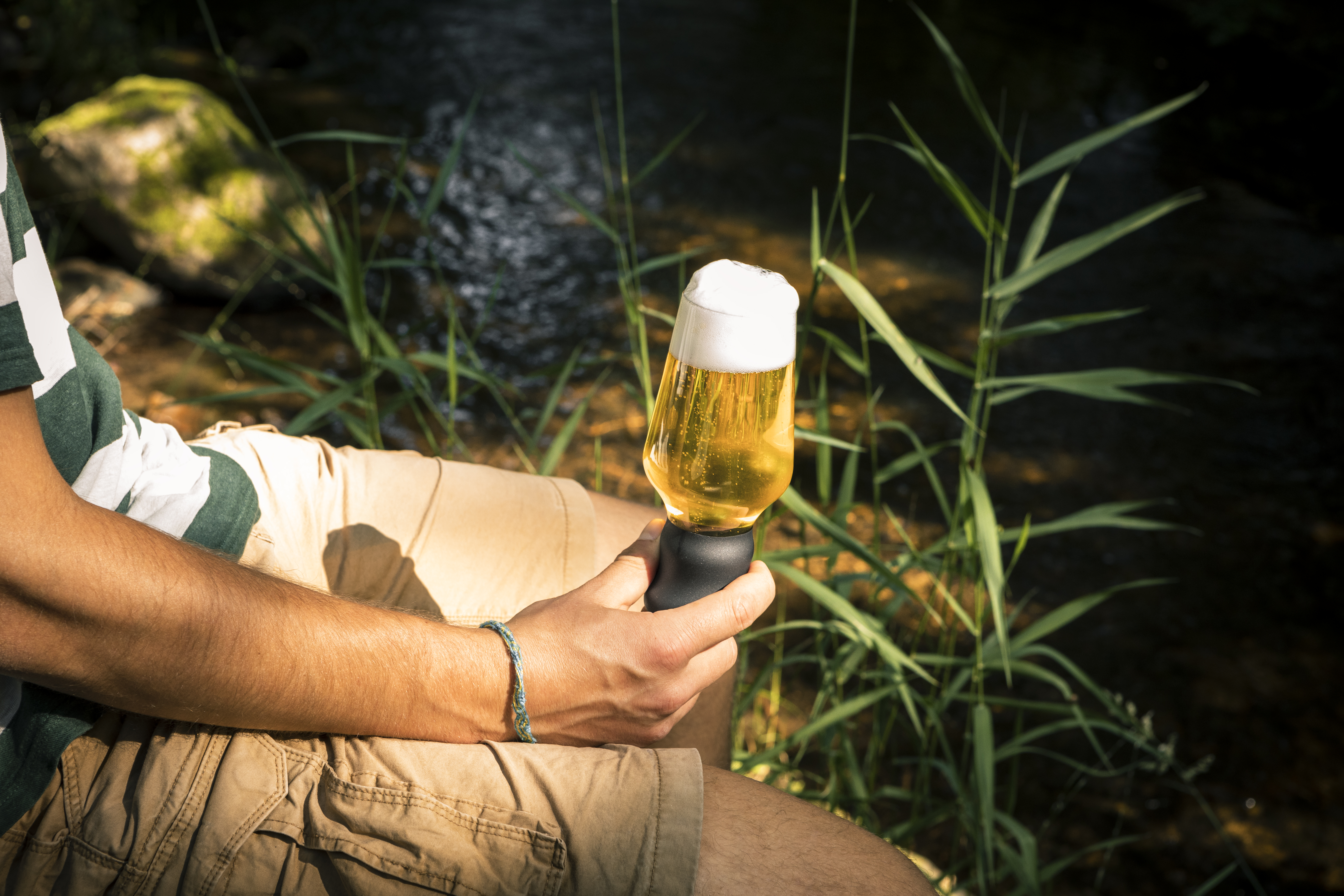 Mann sitzt mit Craft Beer Becher an Fluss