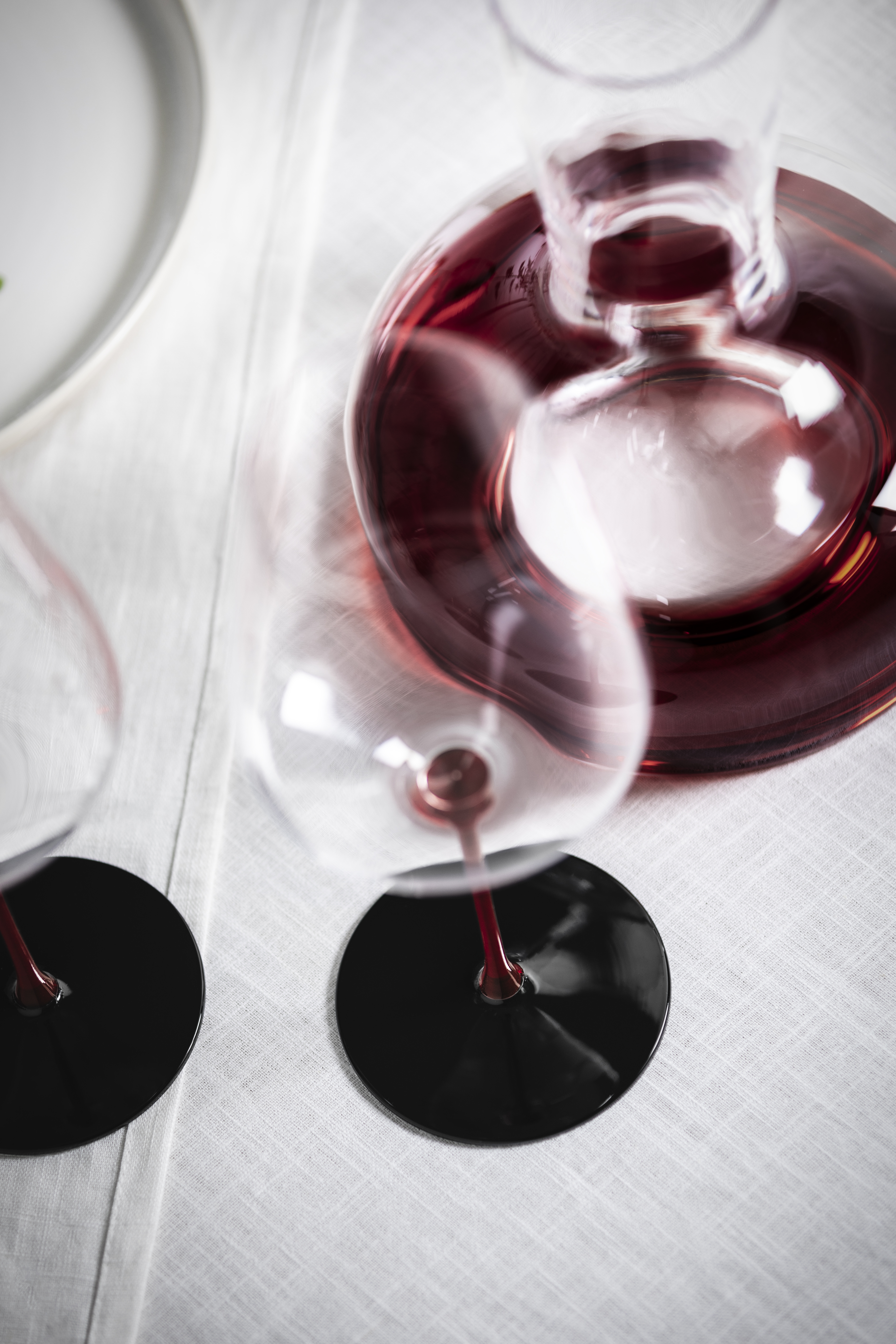 Wine glass with black base and red stem next to decanter